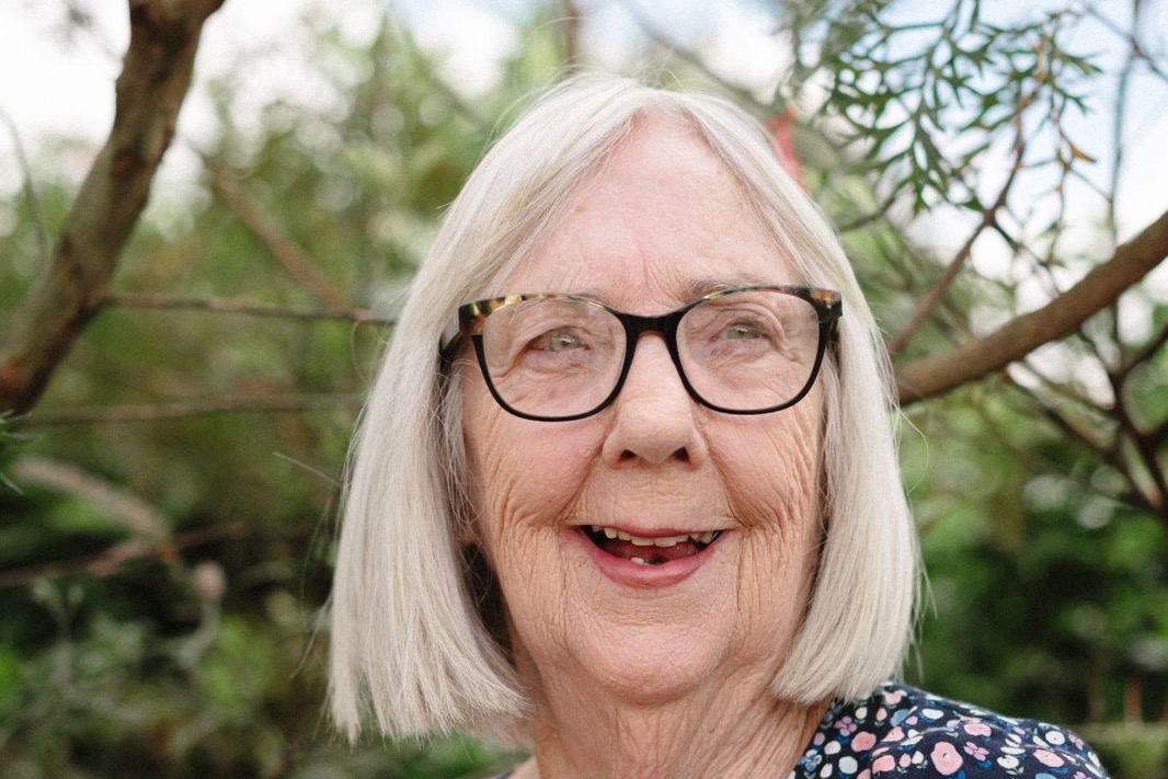 An older woman standing outdoors among native trees
