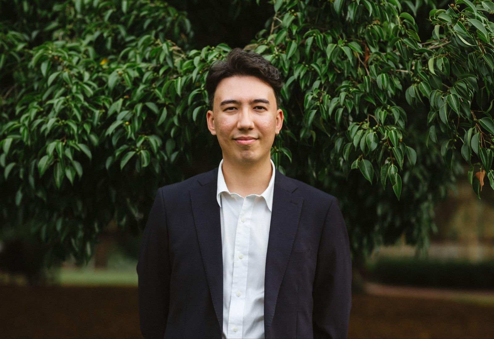 A man in a suit standing in front of dense green foliage